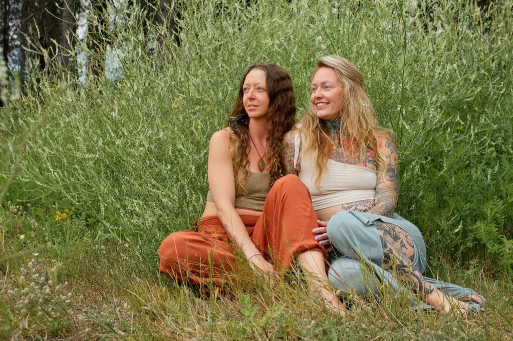 Amanda and Likhita, your retreat hosts, seated together in a mountain meadow